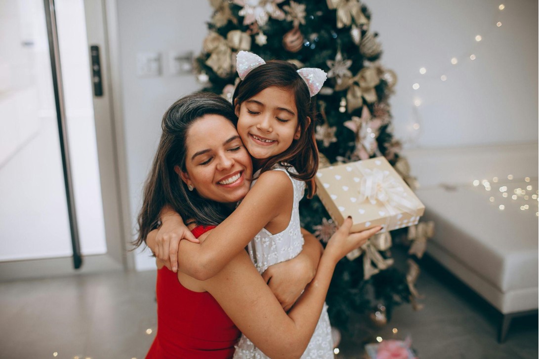Mother and daughter hugging in front of a Christmas tree.